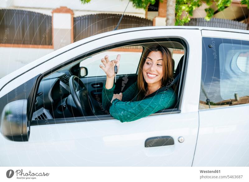 Frau im Inneren eines Autos, die glücklich auf die Schlüssel schaut Autoschlüssel Wagen PKWs Automobil kaufen Kauf lächeln sitzen sitzend sitzt Autokauf Glück