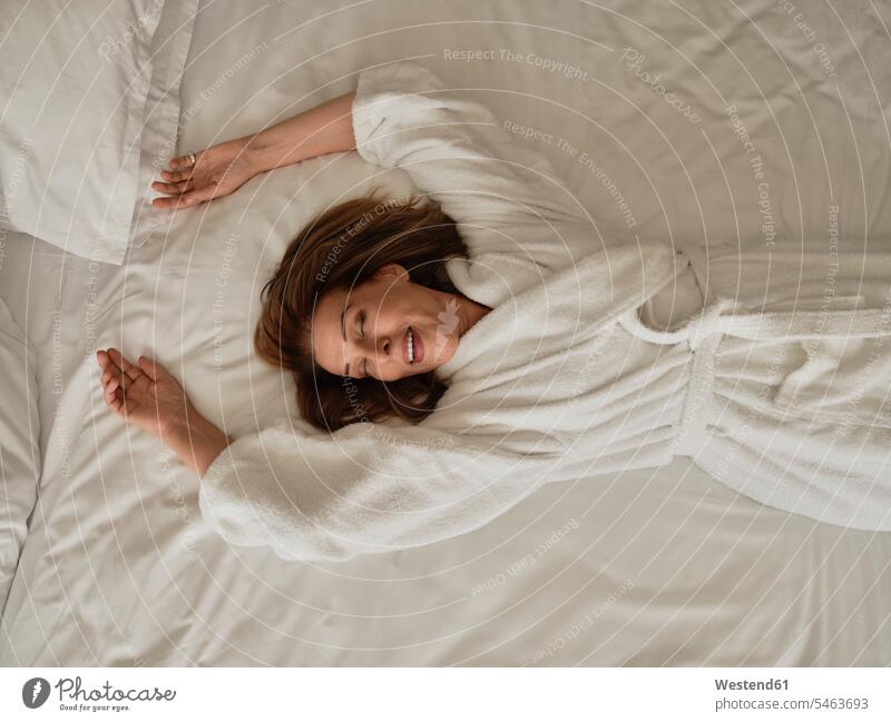 Lächelnde ältere Frau liegt auf weißem Bett in Luxus-Hotelzimmer Farbaufnahme Farbe Farbfoto Farbphoto Innenaufnahme Innenaufnahmen innen drinnen Tag