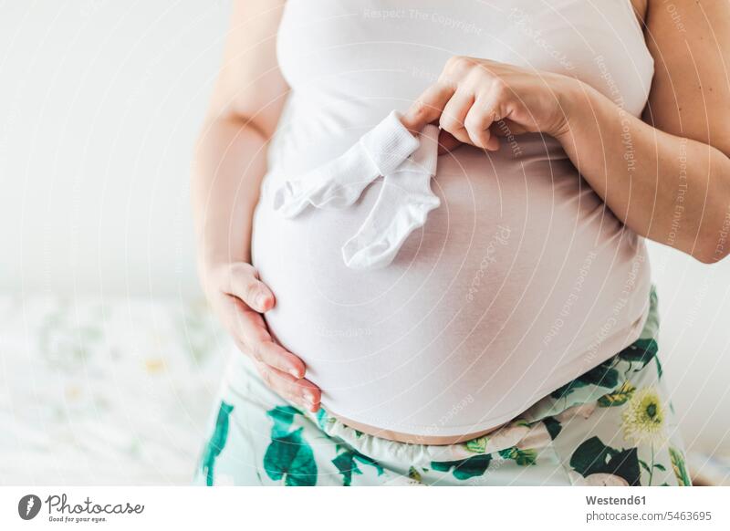 Mittelteil einer schwangeren Frau, die die Socken des Babys hält Strumpf Strümpfe Struempfe Textfreiraum Mittlerer Ausschnitt Mittlere Ausschnitte