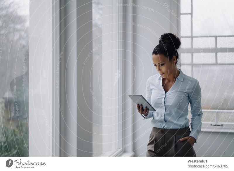 Erfolgreiche Geschäftsfrau, stehend am Fenster, mit digitalem Tablet, lesend Job Berufe Berufstätigkeit Beschäftigung Jobs geschäftlich Geschäftsleben