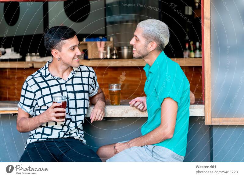 Lächelndes schwules Paar unterhält sich beim Biertrinken am Bartresen Farbaufnahme Farbe Farbfoto Farbphoto Außenaufnahme außen draußen im Freien Tag