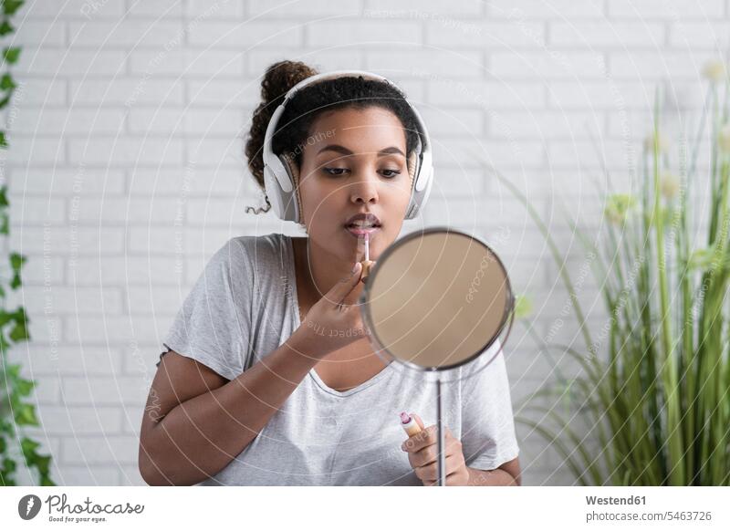 Junge Frau, die zu Hause über Kopfhörer Musik hört und Lipgloss aufträgt Farbaufnahme Farbe Farbfoto Farbphoto Spanien schöne Frau schöne Frauen Mensch Menschen