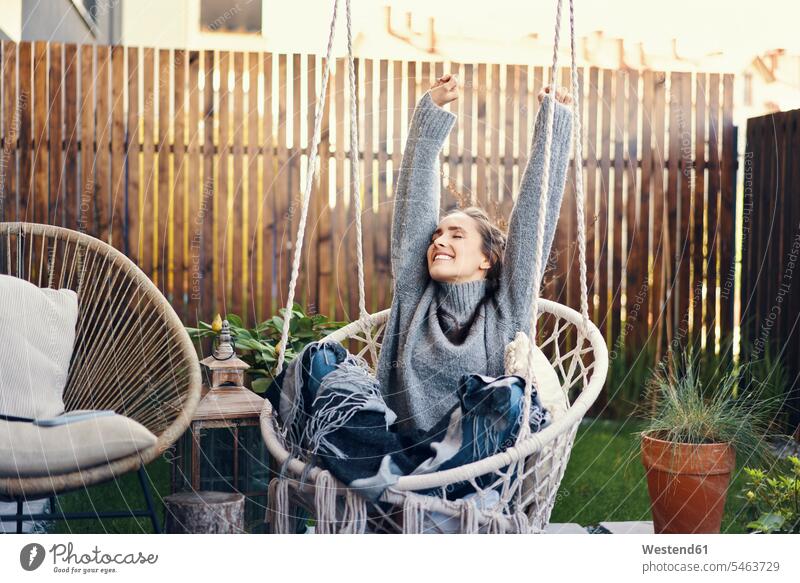 Glückliche junge Frau mit erhobenen Armen entspannt auf der Schaukel im Hof Farbaufnahme Farbe Farbfoto Farbphoto Freizeitbeschäftigung Muße Zeit Zeit haben
