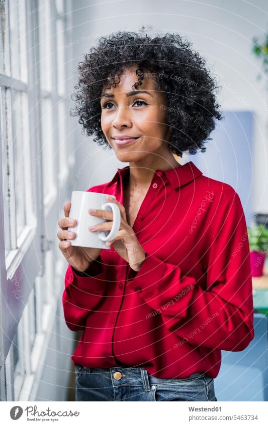 Lächelnde Frau mit Tasse Kaffee schaut aus dem Fenster zu Hause Kaffeetasse Kaffeetassen lächeln weiblich Frauen Zuhause daheim schauen sehend Getränk Getraenk