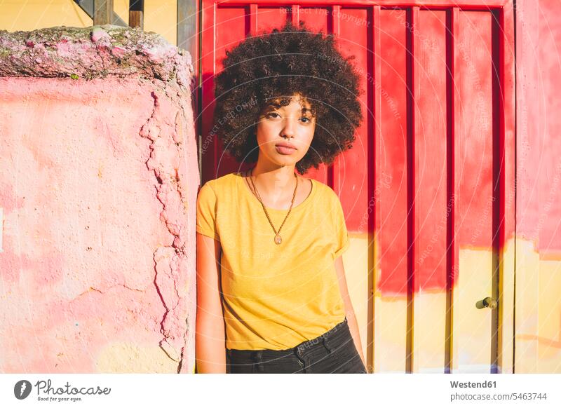 Porträt einer jungen Frau mit Afrofrisur, die an einer Wand lehnt Leute Menschen People Person Personen gelockt gelockte Haare gelocktes Haar lockig