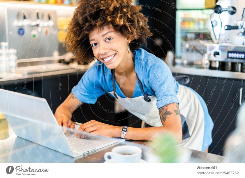 Glückliche Besitzerin mit Laptop am Tresen im Café Farbaufnahme Farbe Farbfoto Farbphoto Innenaufnahme Innenaufnahmen innen drinnen Tag Tageslichtaufnahme