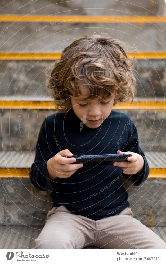 Junge sitzt auf der Treppe und spielt mit Handheld-Spielkonsole Handehelds Buben Knabe Jungen Knaben männlich Konsole Treppenaufgang spielen sitzen sitzend Kind