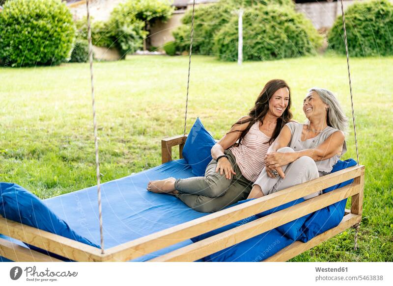Zwei glückliche Frauen entspannen auf einem hängenden Bett im Garten entspannt entspanntheit relaxt weiblich Hängematte Hängematten Freundinnen Betten Gärten