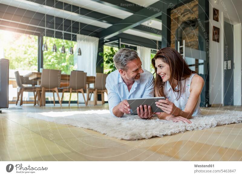 Glückliches Paar liegt zu Hause auf einem Teppich und teilt sich eine Tablette Teppiche Pärchen Paare Partnerschaft Teilen Sharing liegen liegend Zuhause daheim