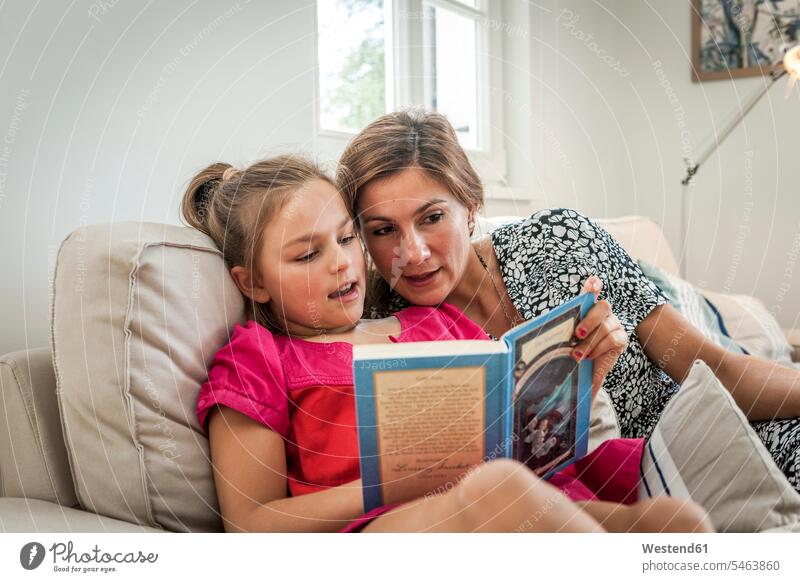Mutter liest Buch mit Tochter auf der Couch im Wohnzimmer Bücher Couches Liege Sofas Lektüre sitzend sitzt reden entspannen relaxen entspanntheit relaxt behüten