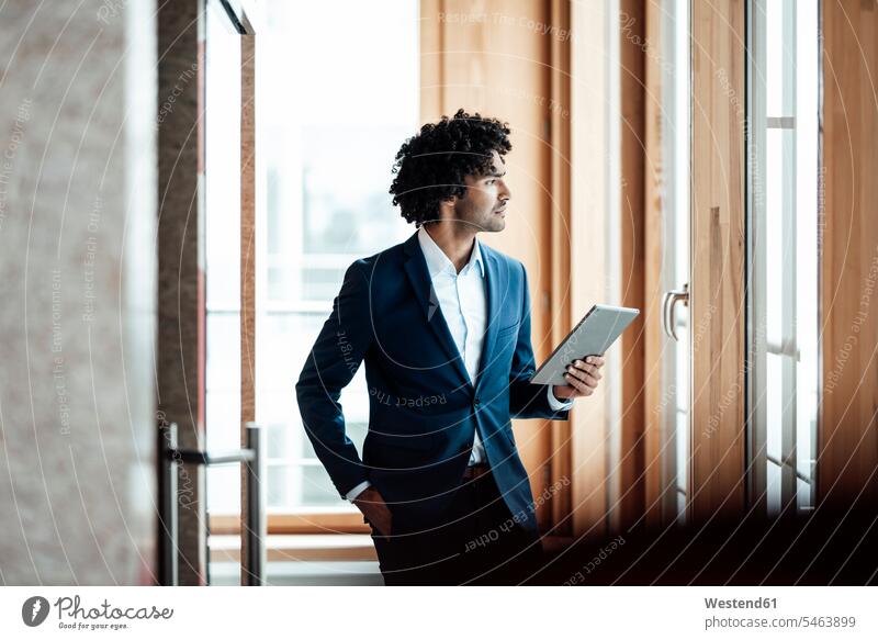 Nachdenklicher männlicher Unternehmer, der ein digitales Tablet hält, während er am Arbeitsplatz wegschaut Farbaufnahme Farbe Farbfoto Farbphoto Deutschland
