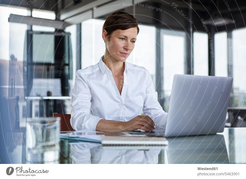 Geschäftsfrau, die im Büro am Glastisch sitzt und einen Laptop benutzt sitzen sitzend Notebook Laptops Notebooks Geschäftsfrauen Businesswomen Businessfrauen