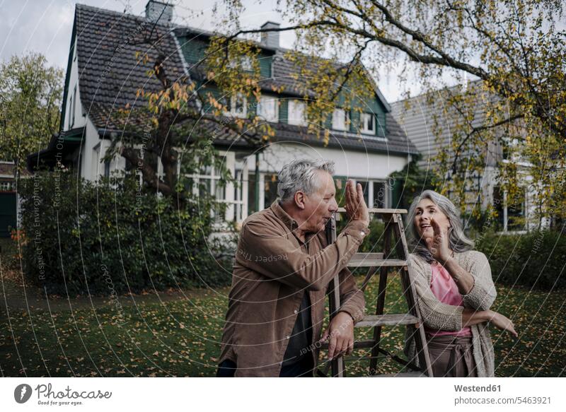 Älteres Ehepaar mit einer Leiter im Garten seines Hauses entspannen relaxen Jahreszeiten entspanntheit relaxt freuen Frohsinn Fröhlichkeit Heiterkeit geniessen