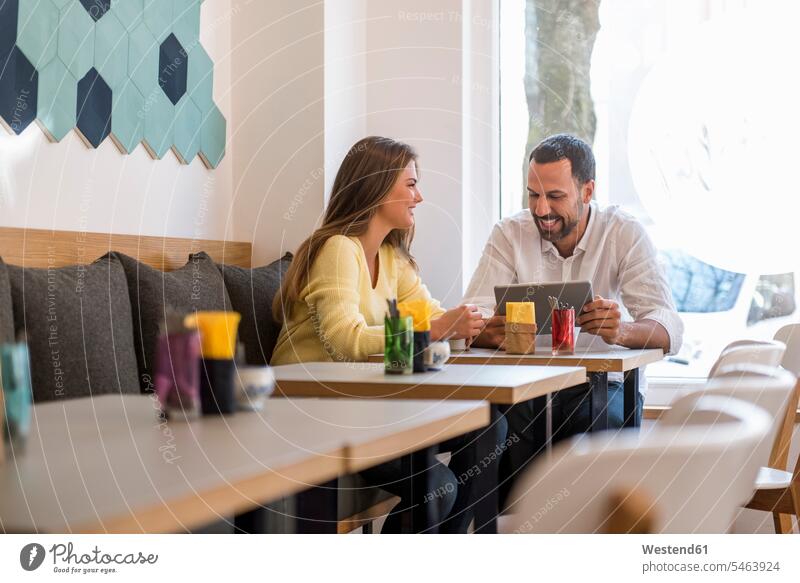 Junge Frau und glücklicher Mann mit Tablette in einem Cafe Männer männlich Kaffeehaus Bistro Cafes Café Cafés Kaffeehäuser weiblich Frauen Glück glücklich sein