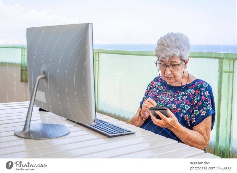 Ältere Frau mit Smartphone auf der Terrasse Tische Rechner Desktop Desktop PC Personal Computer Personal Computers Telekommunikation telefonieren Handies Handys