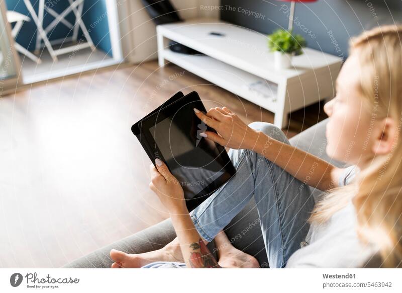 Junge Frau sitzt auf der Couch und benutzt ein Tablet Sofa Couches Liege Sofas weiblich Frauen sitzen sitzend Tablet Computer Tablet-PC Tablet PC iPad