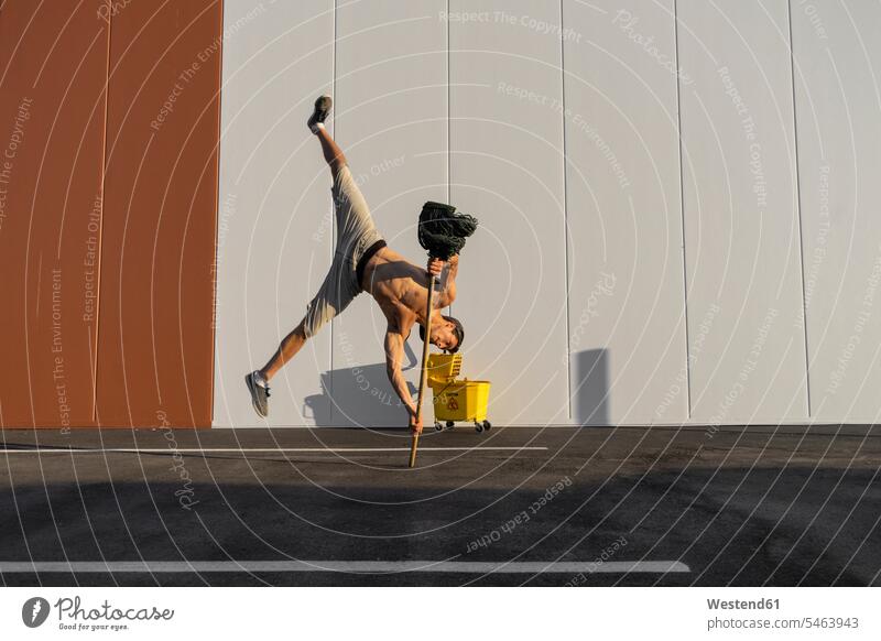 Acrobat spielt mit Putzeimer und Mopp Wischmopp balancieren Akrobat Eimer Trainieren Balance Schwierigkeiten Schatten gelb Choreographie kämpfen