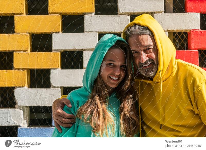 Lächelnder Vater und Tochter stehen an Ziegelmauer Farbaufnahme Farbe Farbfoto Farbphoto Außenaufnahme außen draußen im Freien Tag Tageslichtaufnahme