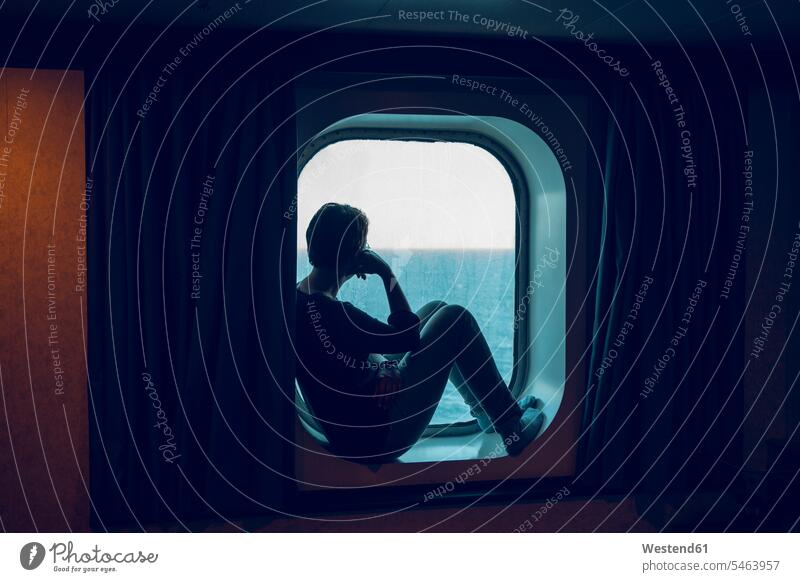 Frau schaut auf die Aussicht, während sie am Schiffsfenster sitzt Farbaufnahme Farbe Farbfoto Farbphoto Innenaufnahme Innenaufnahmen innen drinnen Tag
