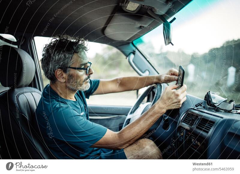 Reifer Mann sitzt in seinem Geländewagen und checkt sein Smartphone Leute Menschen People Person Personen Europäisch Kaukasier kaukasisch 1 Ein ein Mensch