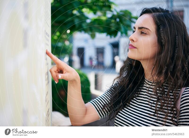 Junge Frau prüft Fahrplan der öffentlichen Verkehrsmittel Stadt staedtisch städtisch schön weiblich Frauen Portrait Porträts Portraits Außenaufnahme draußen