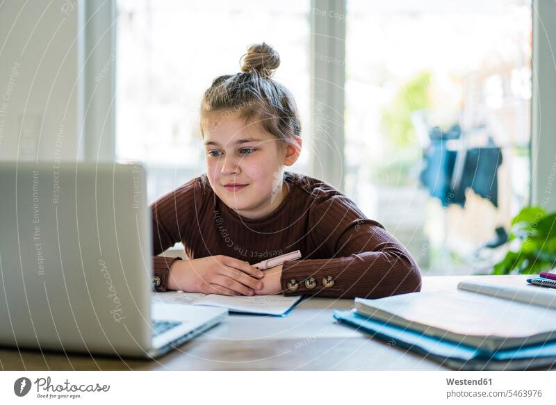 Mädchen mit Buch, das beim Lernen zu Hause einen Laptop benutzt Farbaufnahme Farbe Farbfoto Farbphoto Innenaufnahme Innenaufnahmen innen drinnen Tag
