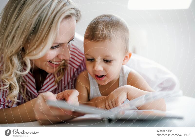 Lächelnde Mutter und Kleinkind Sohn liegen im Bett zu Hause ein Buch lesen Zuhause lächeln Eltern Familie Mensch Kind Nahaufnahme nebeneinander Fürsorge morgens