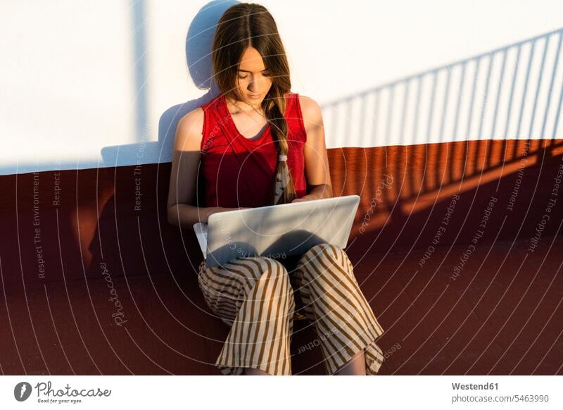 Teenager-Mädchen sitzt im Freien im Sonnenlicht mit Laptop sitzen sitzend Notebook Laptops Notebooks Teenagerin junges Mädchen Teenagerinnen weiblich junge Frau
