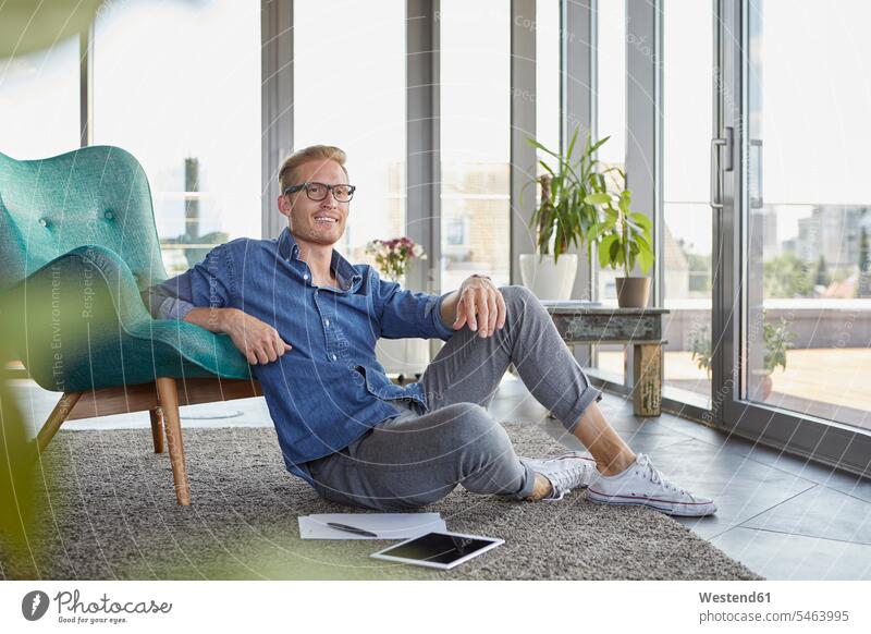 Lächelnder junger Mann sitzt auf Teppich mit Tablet und Notizblöcke zu Hause Tablet Computer Tablet-PC Tablet PC iPad Tablet-Computer Notizzettel Zuhause daheim