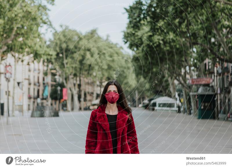 Porträt einer Frau mit roter Gesichtsmaske und Jacke, die auf einer leeren Straße in der Stadt steht, Barcelona, Spanien Farbaufnahme Farbe Farbfoto Farbphoto