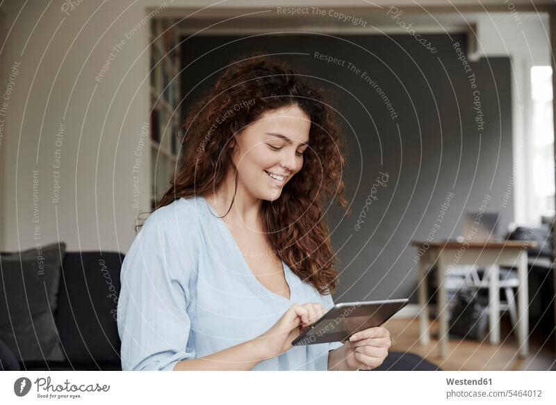 Lächelnde Frau benutzt digitales Tablett zu Hause Farbaufnahme Farbe Farbfoto Farbphoto Innenaufnahme Innenaufnahmen innen drinnen Tag Tageslichtaufnahme