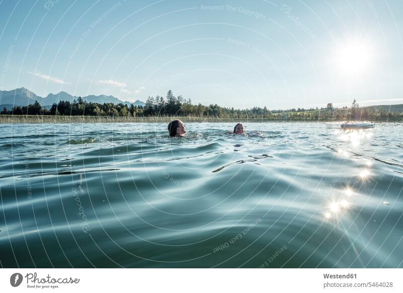 Zwei Mädchen schwimmen bei Sonnenschein in einem See, Bannwaldsee, Allgäu, Bayern, Deutschland Tagaufnahme Fokus auf den Vordergrund Fokus auf dem Vordergrund