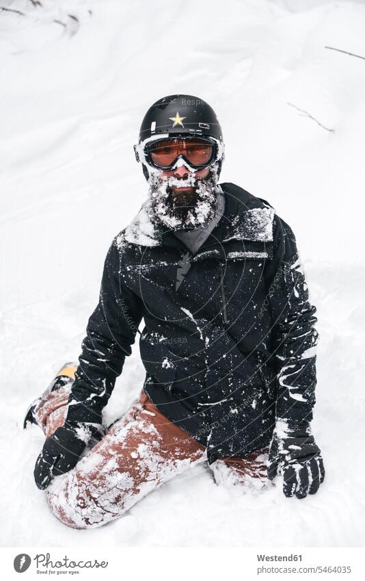 Schneebedeckter junger Mann in Skikleidung kniend im Schnee verschneit schneebedeckt Skianzug Skianzüge Skibekleidung Schianzug Männer männlich Skifahren