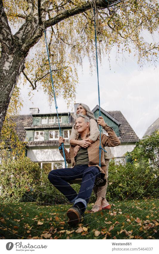 Glückliche Frau umarmt älteren Mann auf einer Schaukel im Garten Schaukeln entspannen relaxen Arm umlegen Umarmung Umarmungen Jahreszeiten entspanntheit relaxt