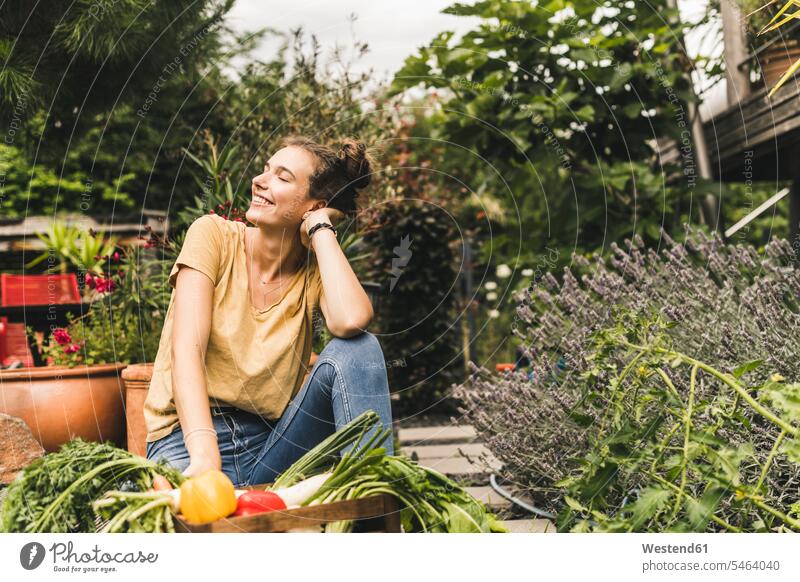 Junge Frau mit geschlossenen Augen sitzt bei Gemüse und Pflanzen im Gemeinschaftsgarten Farbaufnahme Farbe Farbfoto Farbphoto Deutschland Freizeitbeschäftigung