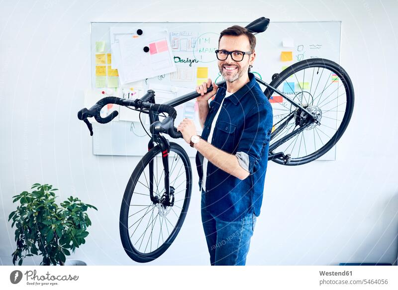 Porträt eines lächelnden Geschäftsmannes mit Fahrrad im Büro Office Büros Bikes Fahrräder Räder Rad Portrait Porträts Portraits tragen transportieren