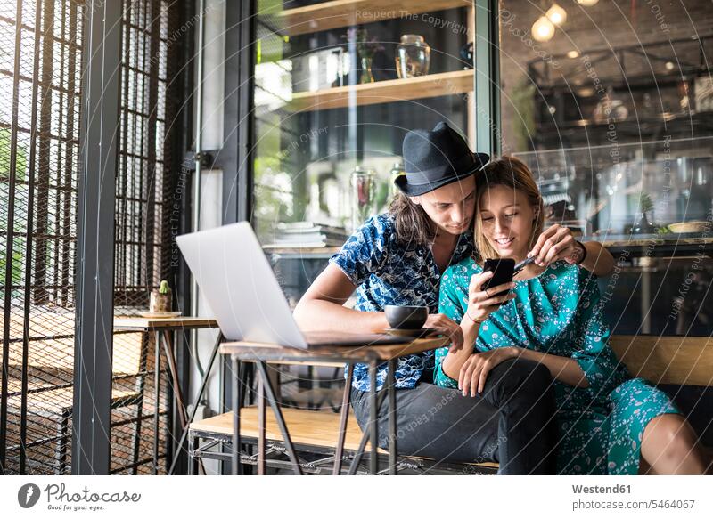 Künstlerpaar, das im Café sitzt und das Smartphone der jungen Frau überprüft verliebt Zuneigung Cafe Kaffeehaus Bistro Cafes Cafés Kaffeehäuser iPhone