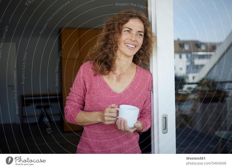 Frau mit Kaffeetasse lächelt, während sie sich zu Hause an die Tür lehnt Farbaufnahme Farbe Farbfoto Farbphoto Tag Tageslichtaufnahme Tageslichtaufnahmen