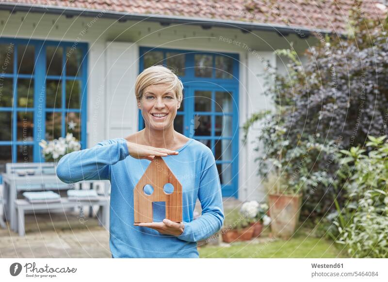 Porträt einer lächelnden Frau, die vor ihrem Haus haltenden Hausmodell steht weiblich Frauen Modell Modelle Portrait Porträts Portraits stehen stehend Häuser