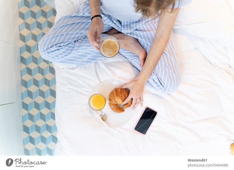 Junge Frau sitzt auf dem Bett und trinkt einen Kaffee Gläser Trinkglas Trinkgläser Betten Telekommunikation telefonieren Handies Handys Mobiltelefon