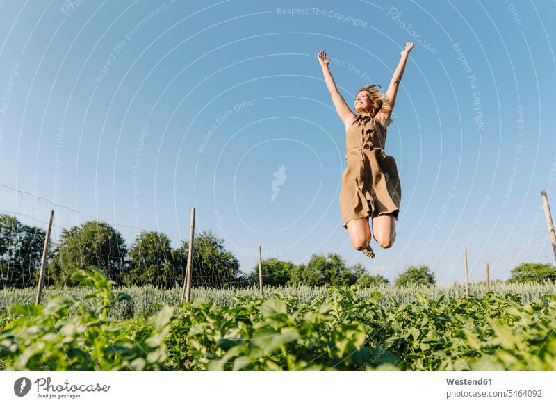Glückliche junge Frau springt in ein Gemüsebeet Kleider begeistert Enthusiasmus enthusiastisch Überschwang Überschwenglichkeit freuen glücklich sein