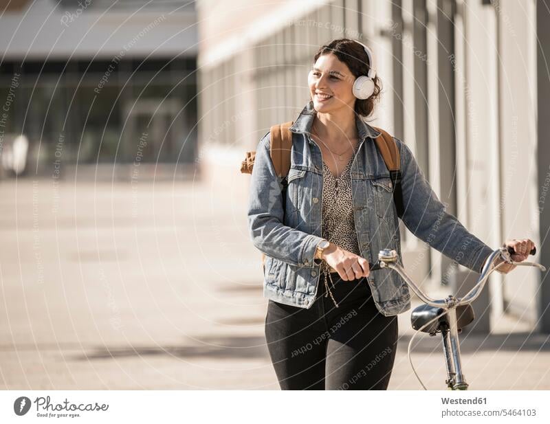 Lächelnde Pendlerin hört Musik, während sie mit dem Fahrrad auf der Straße in der Stadt unterwegs ist Farbaufnahme Farbe Farbfoto Farbphoto Deutschland