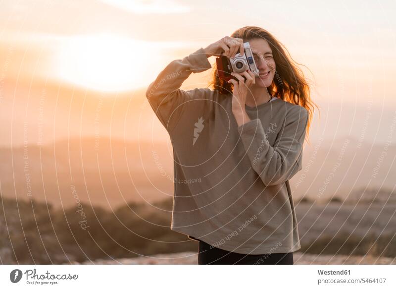 Spanien, Barcelona, Naturpark von Sant Llorenc, Frau nimmt ein Bild mit Vintage-Kamera bei Sonnenuntergang weiblich Frauen Sonnenuntergänge fotografieren