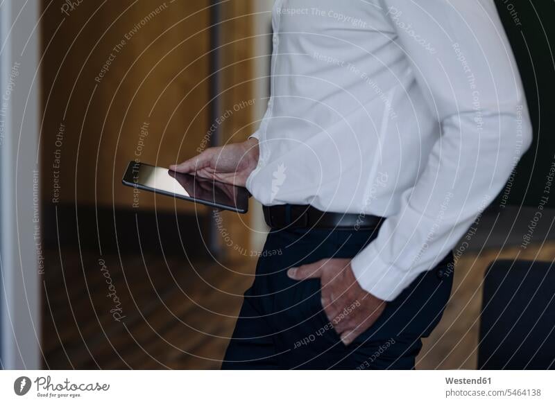 Geschäftsmann mit Händen in den Taschen, der ein digitales Tablet hält, während er im Büro steht Farbaufnahme Farbe Farbfoto Farbphoto Innenaufnahme