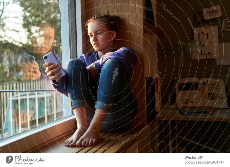 Mädchen sitzt abends barfuss auf dem Fensterbrett und schaut sich ein Smartphone an Informationen Tische Arbeitstisch Schreibtische Telekommunikation Handies