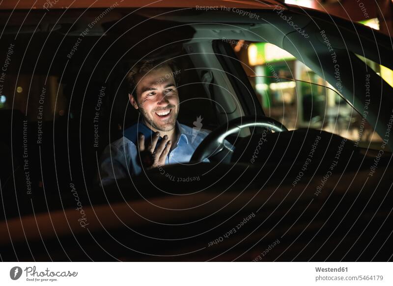 Glücklicher junger Mann mit Handy im Auto bei Nacht Deutschland Anruf zuhören zuhörend Drahtlose Technologie drahtlose Verbindung Drahtlose Kommunikation