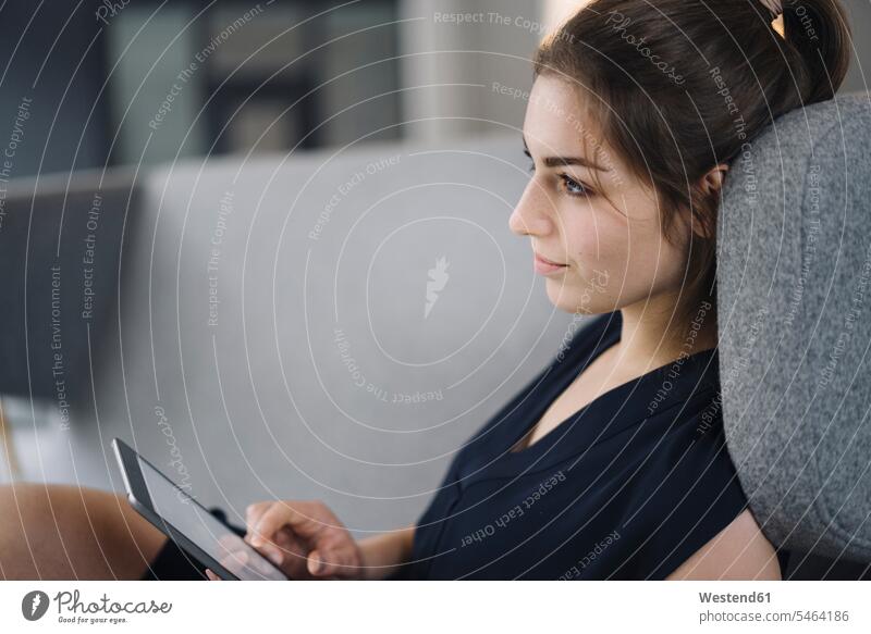 Junge Geschäftsfrau sitzt auf Couch mit digitalem Tablet und schaut in die Ferne Leute Menschen People Person Personen Europäisch Kaukasier kaukasisch 1 Ein