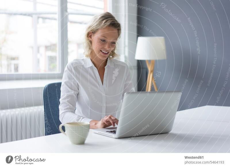 Lächelnde junge Geschäftsfrau mit Laptop am Schreibtisch im Büro Job Berufe Berufstätigkeit Beschäftigung Jobs geschäftlich Geschäftsleben Geschäftswelt
