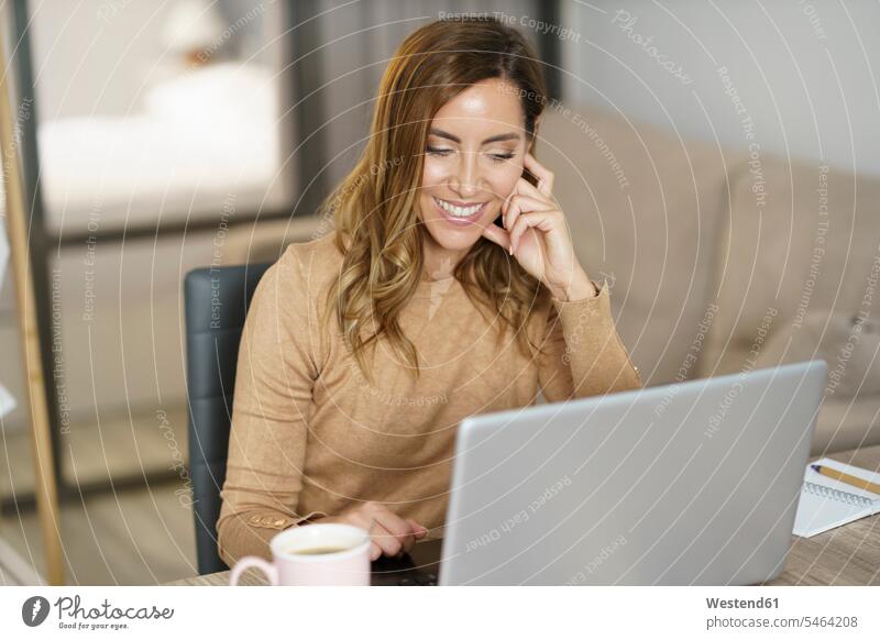 Geschäftsfrau lächelt bei der Arbeit am Laptop zu Hause Farbaufnahme Farbe Farbfoto Farbphoto Innenaufnahme Innenaufnahmen innen drinnen Tag Tageslichtaufnahme