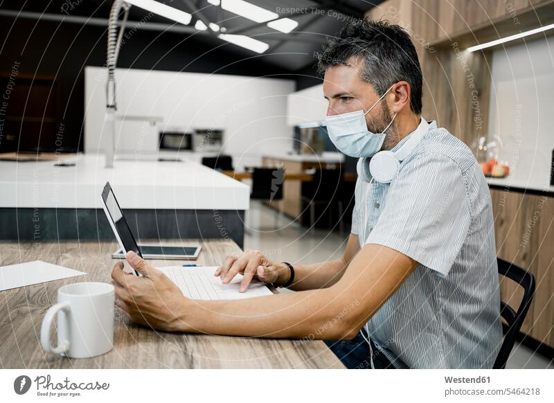Geschäftsmann trägt Schutzmaske, während er während der COVID-19-Pandemie einen Laptop am Schreibtisch im Büro benutzt Farbaufnahme Farbe Farbfoto Farbphoto